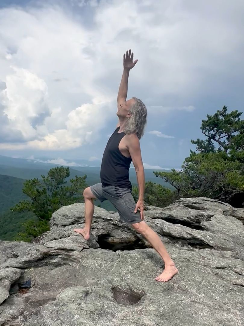 Yoga pose on a mountain ridge above forested hills