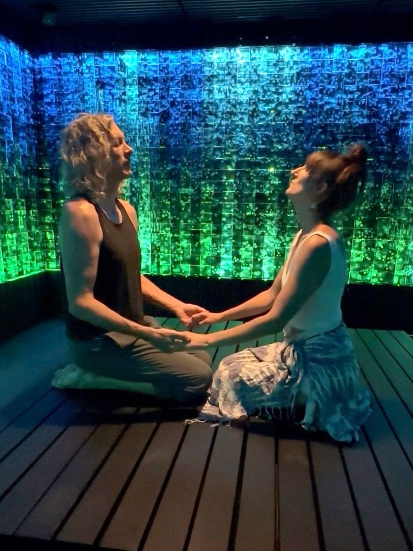 Two people sitting facing each other, hands joined